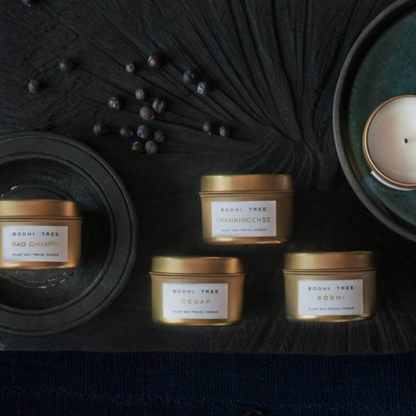 four travel candles in gold colored tin with a black fabric background