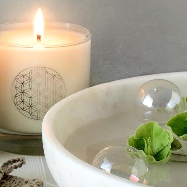 2 glass balls floating in white bowl and lit white bodhi tree candle in background